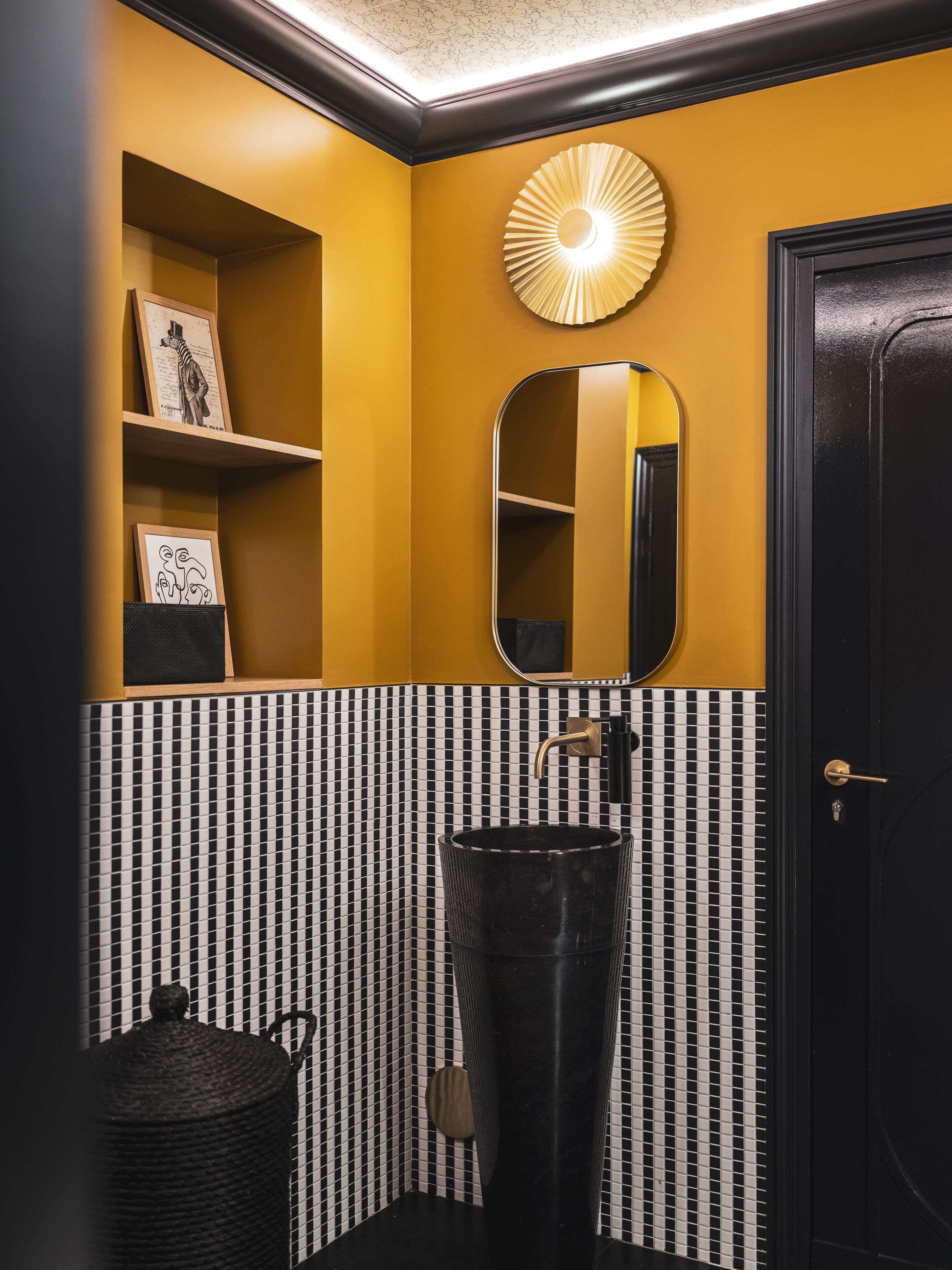 A bathroom with a black door, a mirror, a sink, and shelves with framed pictures.