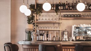 A bar area with a wooden counter, bar stools, and a coffee machine. - Dandy Hotel  (Paris)