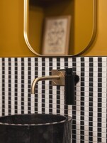 Une salle de bain avec un mur recouvert de carreaux noirs et blancs formant un motif à damier, un robinet doré et un lavabo noir.