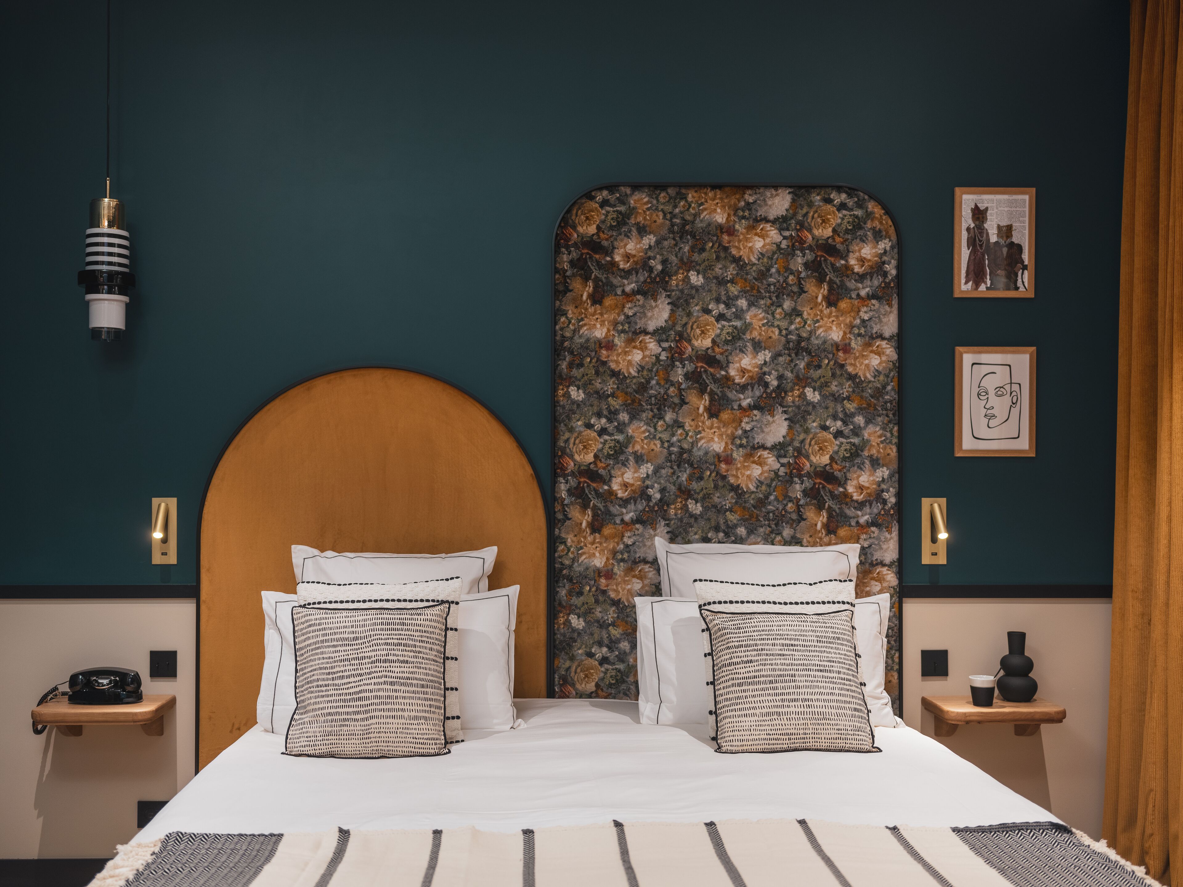 Uma cama de casal com cabeceira de madeira, duas mesas de cabeceira com luminárias e cabeceira estampada com motivos florais.