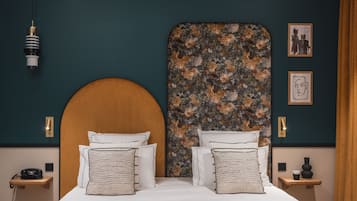 Uma cama de casal com cabeceira de madeira, duas mesas de cabeceira com luminárias e cabeceira estampada com motivos florais.