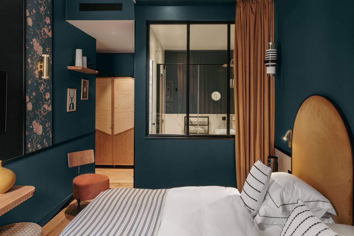 A modern bedroom with a bed, a wooden wardrobe, a vanity, and a large window with curtains.