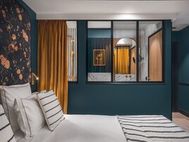 A modern bedroom with a bed, curtains, a window, and a mirror reflecting a bathroom.