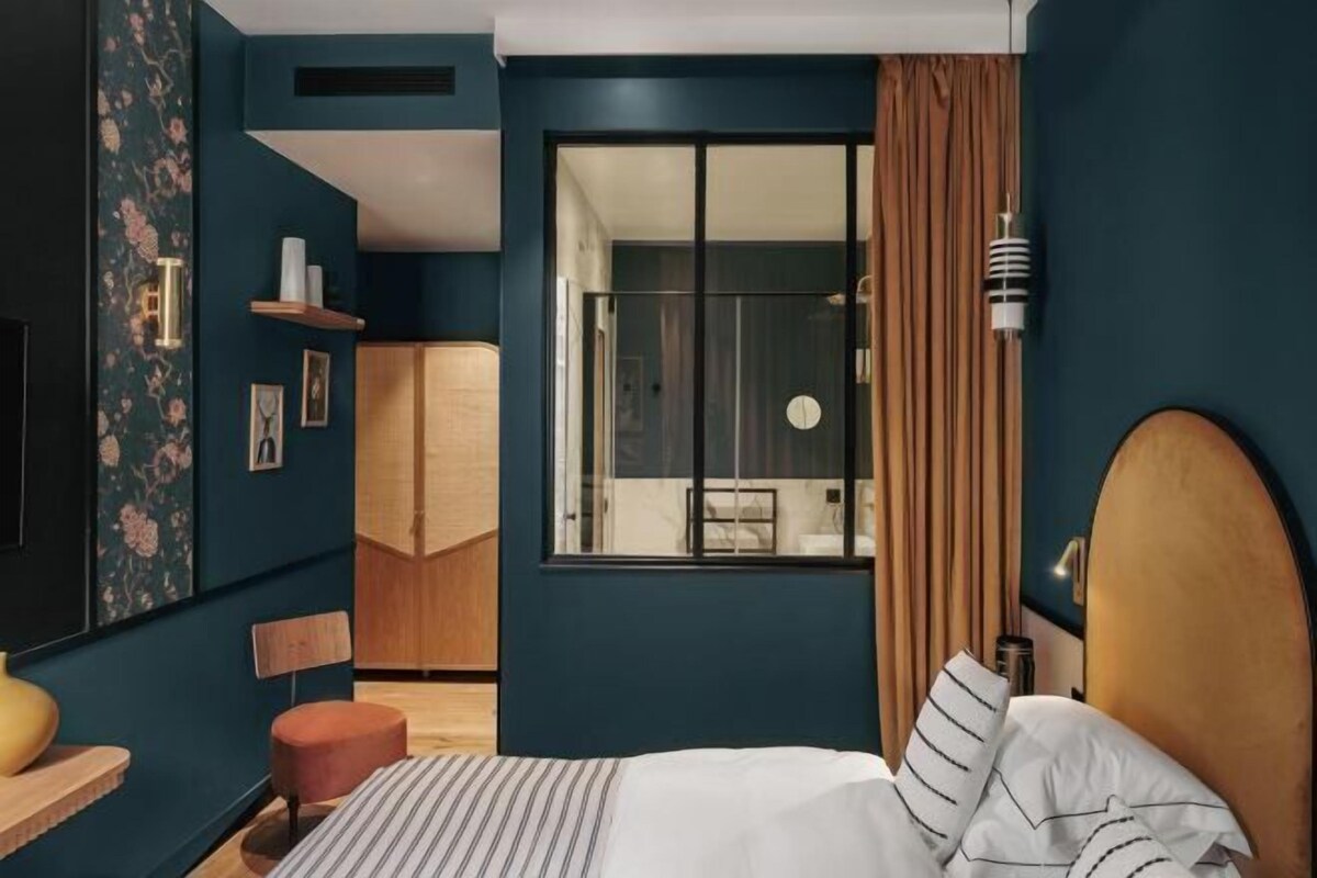A modern hotel room with a bed, a desk, a chair, a wardrobe, and a window with curtains.