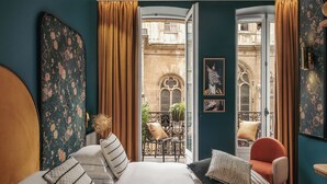 A bedroom with a large bed, two chairs, a view of a courtyard, and a door with zebra artwork. - Dandy Hotel  (Paris)