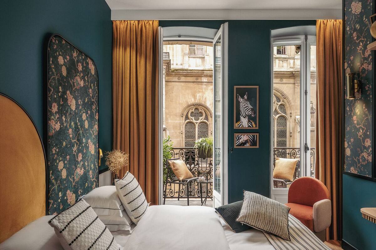 A bedroom with a large bed, two chairs, a view of a courtyard, and a door with zebra artwork.