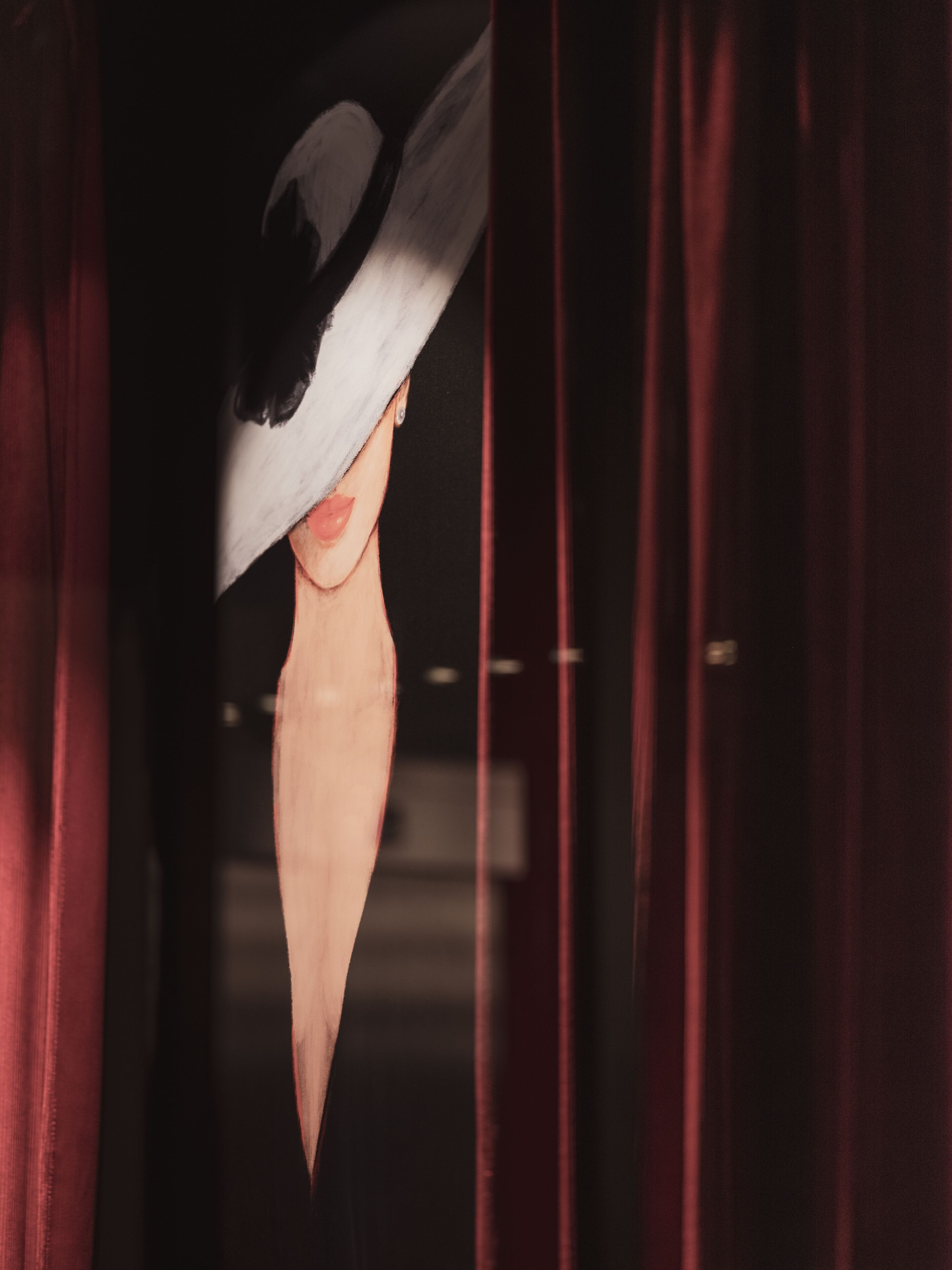 A person wearing a hat with a black and white design, standing in front of red curtains.