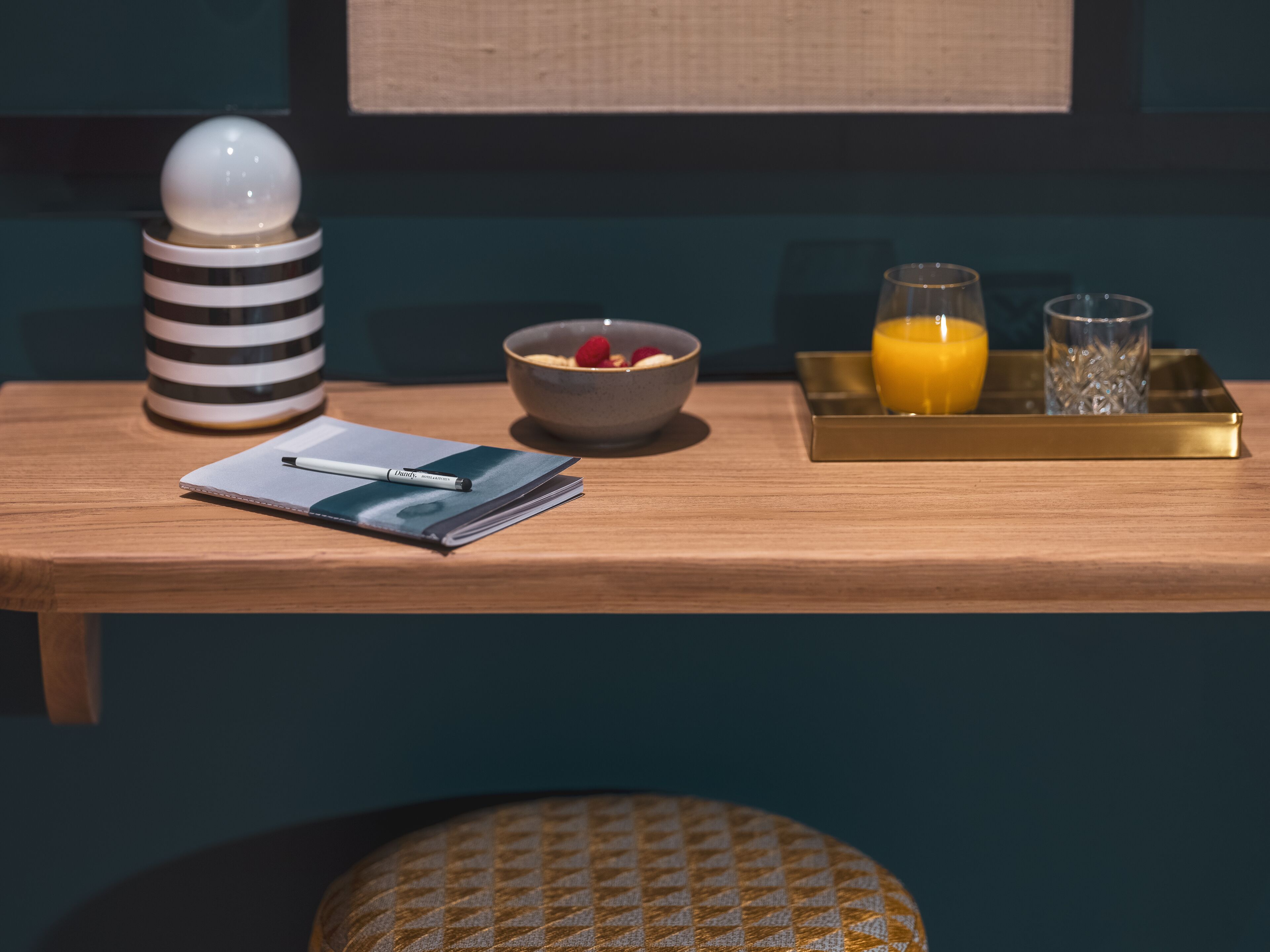 A wooden table with a notebook, pen, bowl of cereal, and a tray with a glass of orange juice and a glass of water.