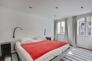 A modern bedroom with a bed, a red blanket, a nightstand, a lamp, and a window with curtains.