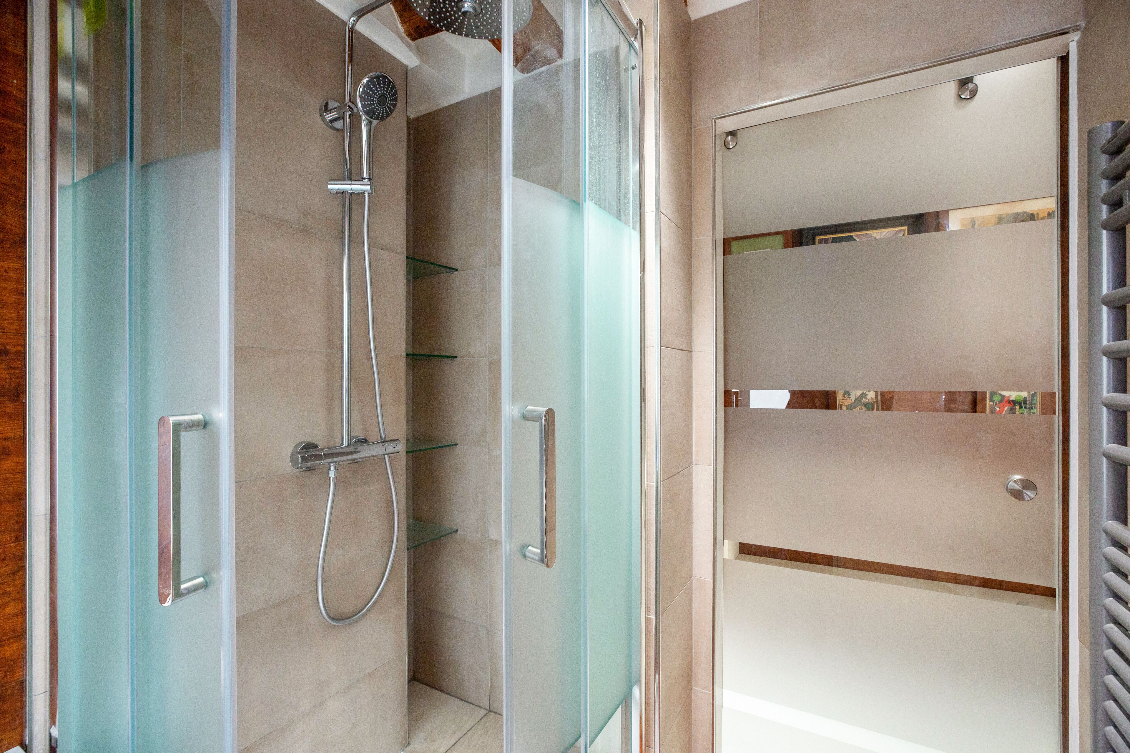 Un baño moderno con ducha envuelta en vidrio, puerta de cristal y estante empotrado.