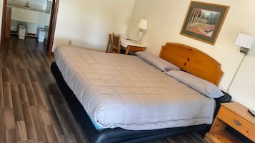 Un dormitorio con cama, cabecera de madera, mesitas de noche, lámpara, un cuadro enmarcado en la pared y un baño a la vista al fondo.