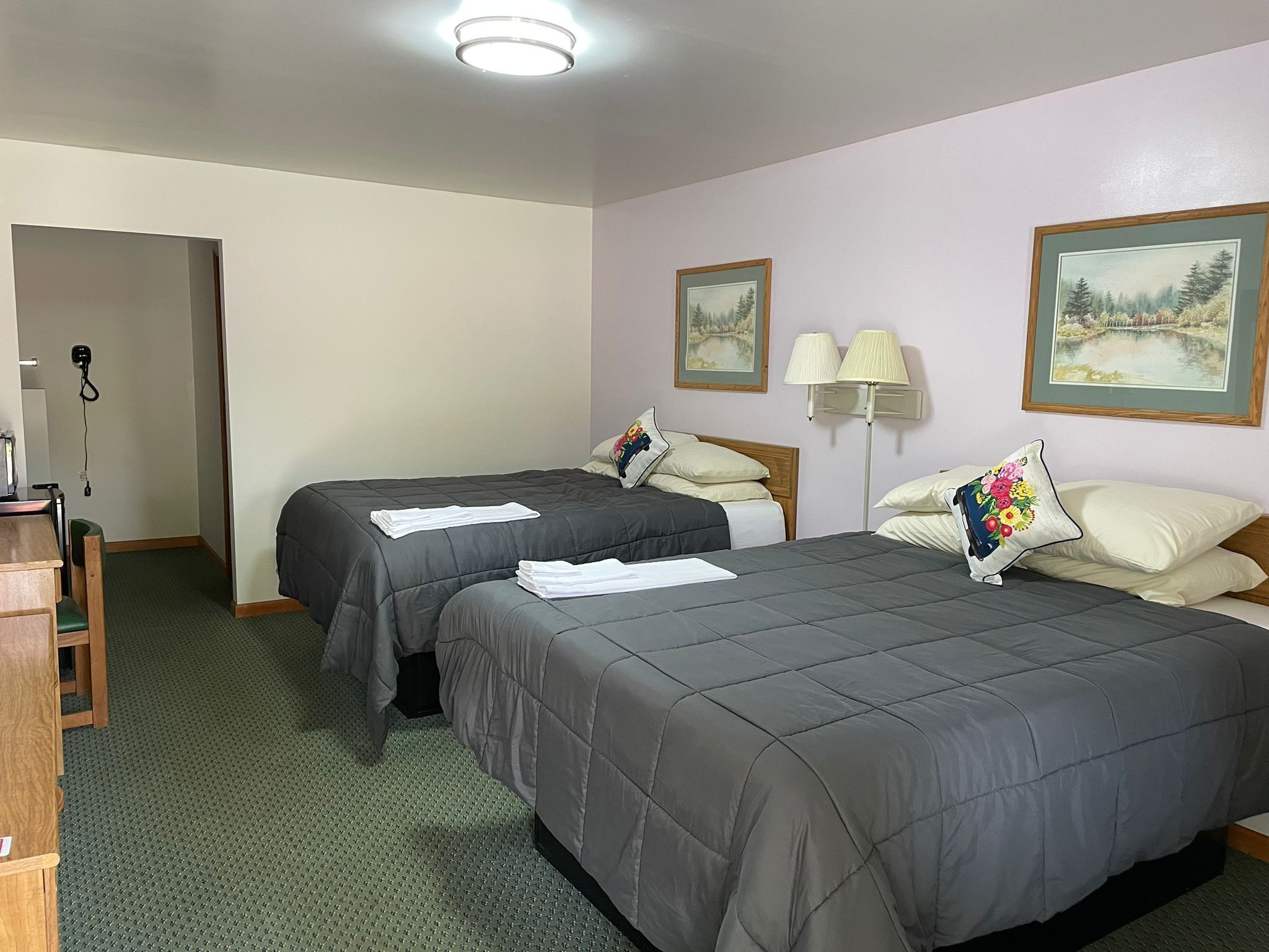 Habitación de hotel con dos camas, un escritorio y una silla. Cuenta con dos lámparas de pared y dos cuadros enmarcados.