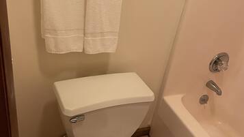 Une salle de bain équipée de toilettes, d’une baignoire et de deux serviettes accrochées au mur.