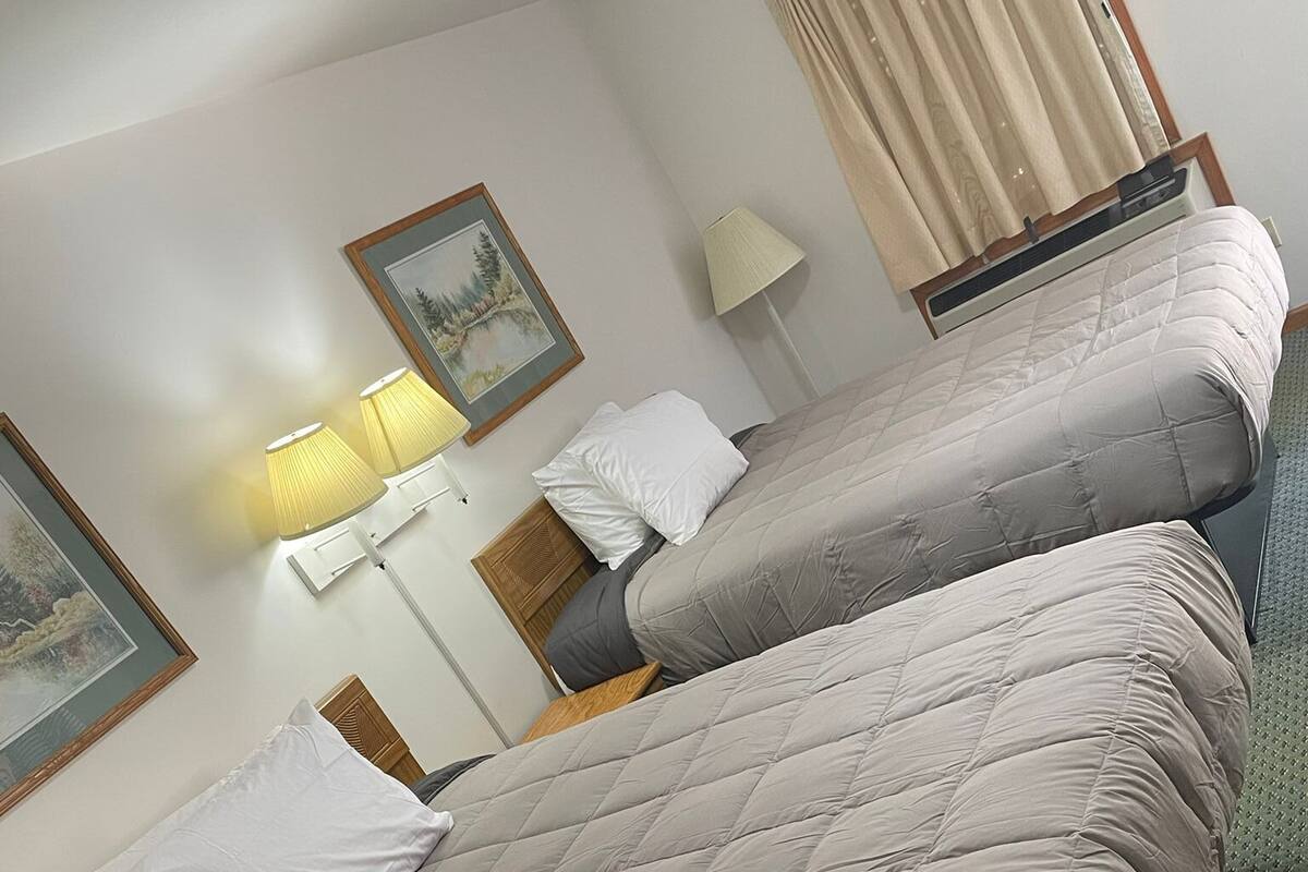 A hotel room with two beds, a nightstand, a lamp, and a painting on the wall.
