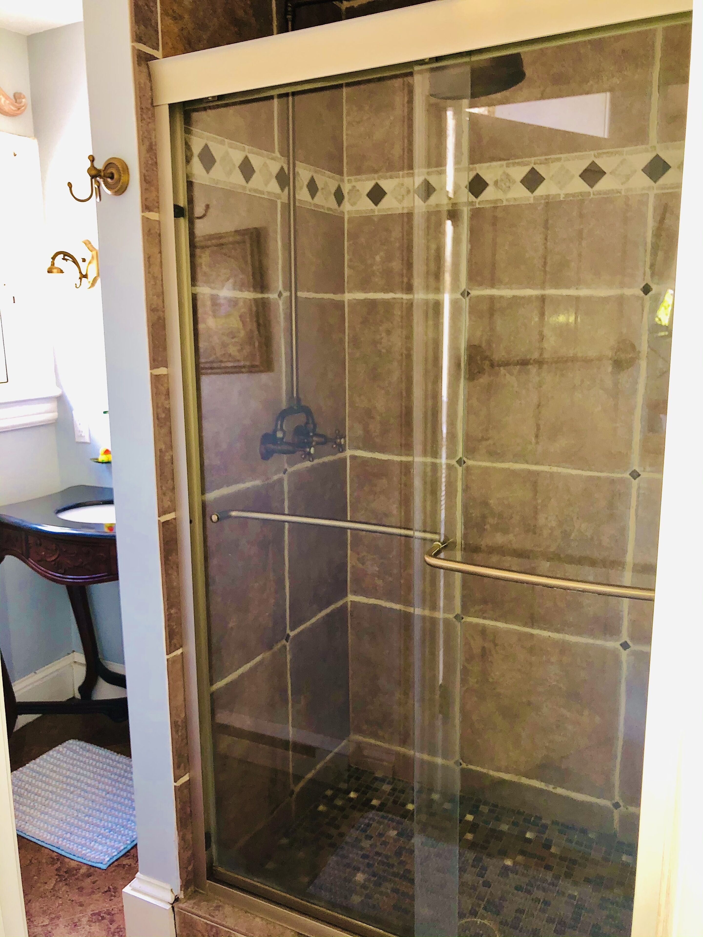 Une douche fermée par des parois de verre, avec un sol carrelé et une poignée en métal.