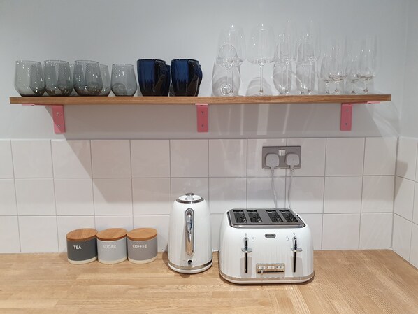 A kitchen with a wooden shelf holding various glassware, a Breville toaster, and three labeled containers on the counter.