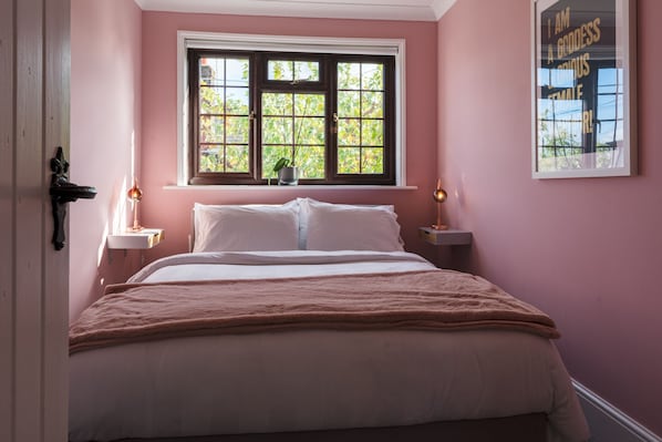 A bedroom with a bed, two bedside tables, a window with a view, and a wall-mounted artwork.