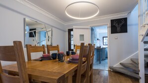 Un coin repas avec une table et des chaises en bois, un luminaire suspendu moderne et une œuvre d’art murale noire.