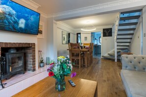 A living room with a fireplace, a TV mounted on the wall, a dining area with wooden furniture, and a staircase.