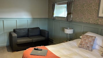 A hotel room with a bed, a sofa, a lamp, and a window with curtains.