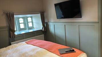 A bedroom with a bed, a window with curtains, a radiator, a television mounted on the wall, and a notebook on the bed.