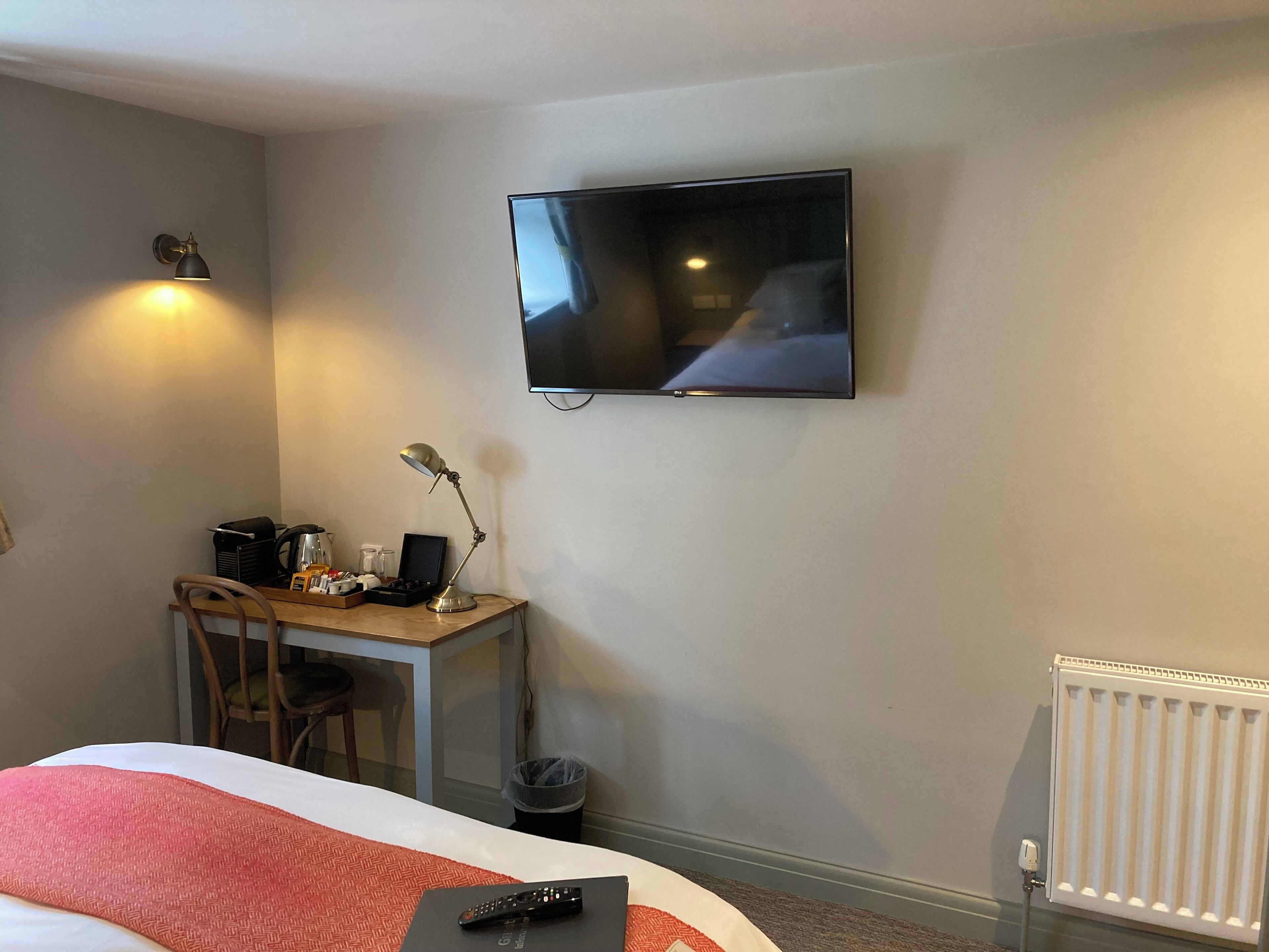 A hotel room with a bed, a desk with a lamp, a television, and a radiator.