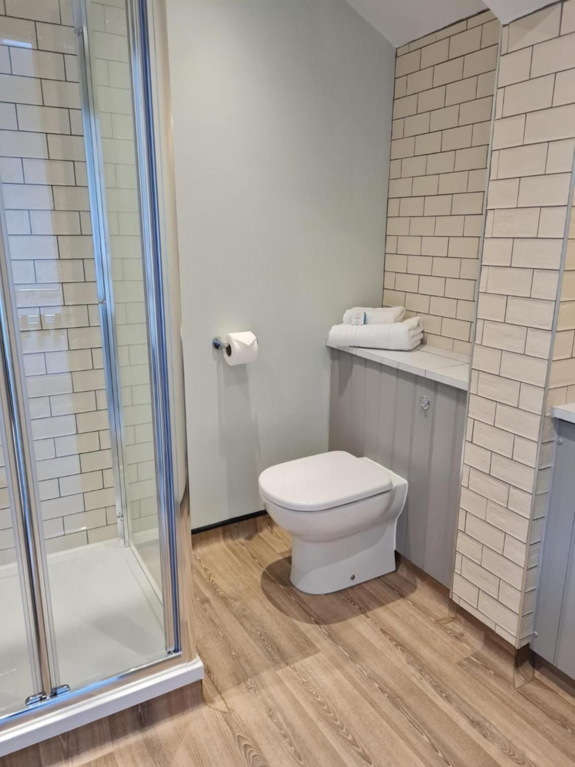 Un baño moderno con inodoro, cabina de ducha y porta papel higiénico.