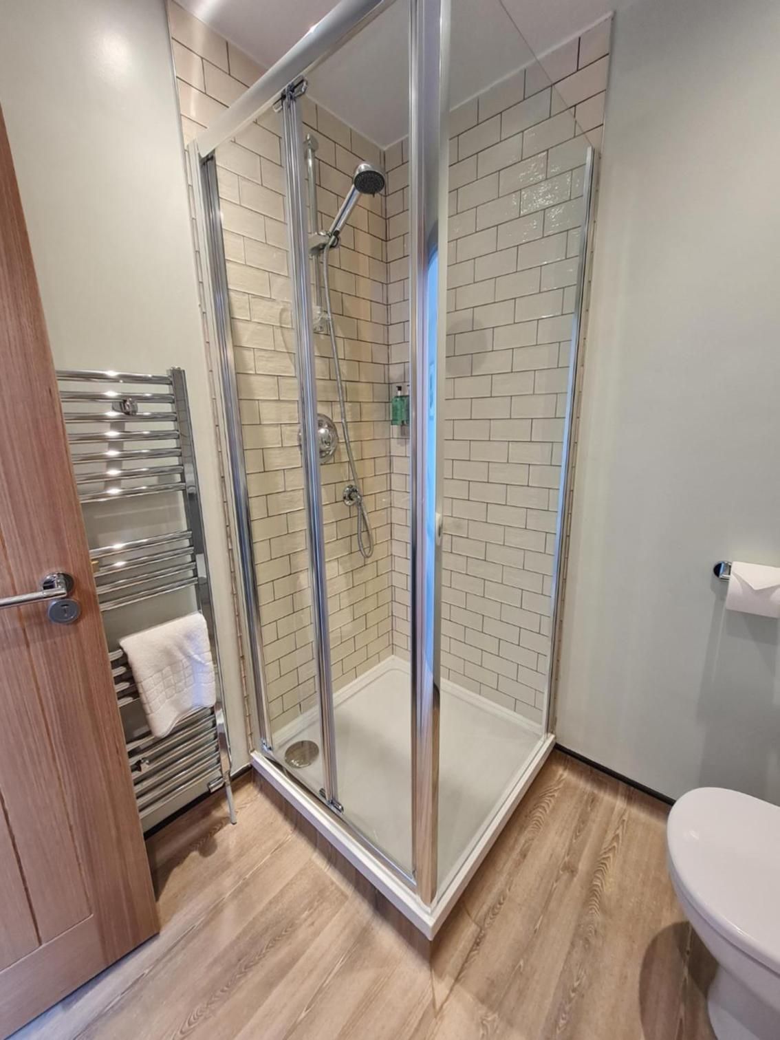 Ein modernes Badezimmer mit einer gläsernen Duschkabine, Holzboden und Toilette.