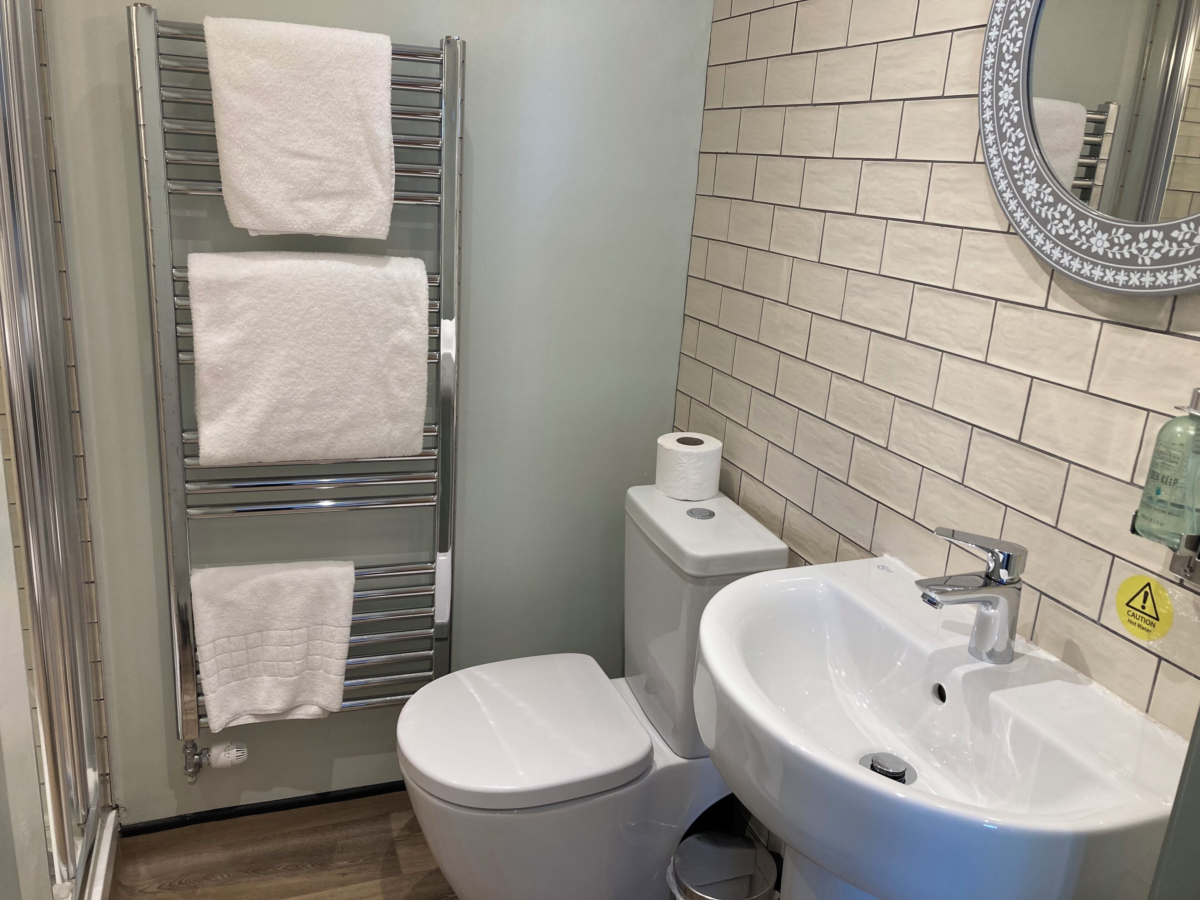 A bathroom with a toilet, a sink, a towel rack with three towels, and a toilet paper roll.