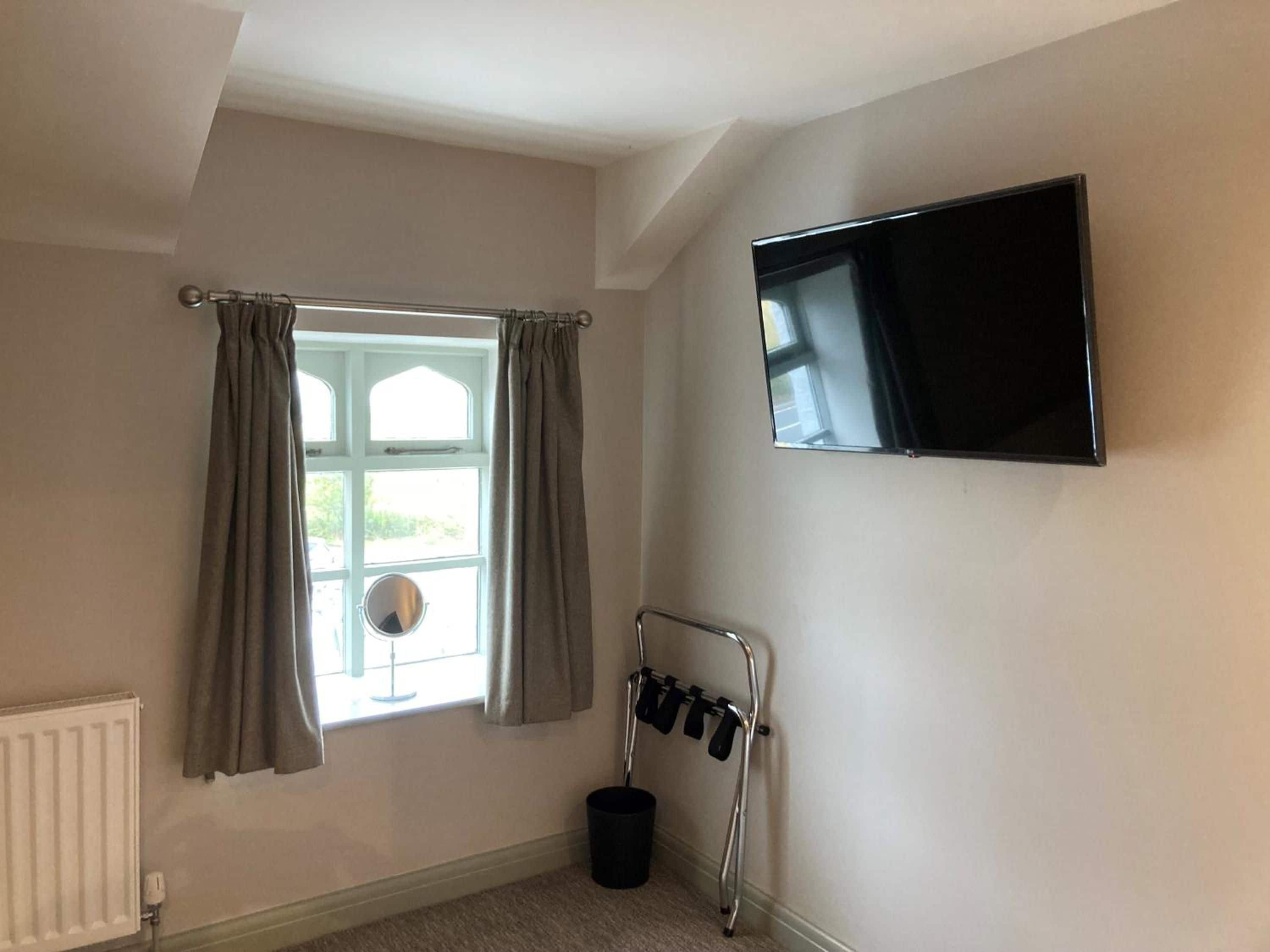 A room with a window, a radiator, a television mounted on the wall, and a shoe rack.