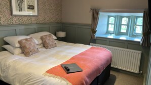 Un lit bien fait, recouvert d’une couverture rouge, une lampe de chevet et un tableau encadré accroché au mur.