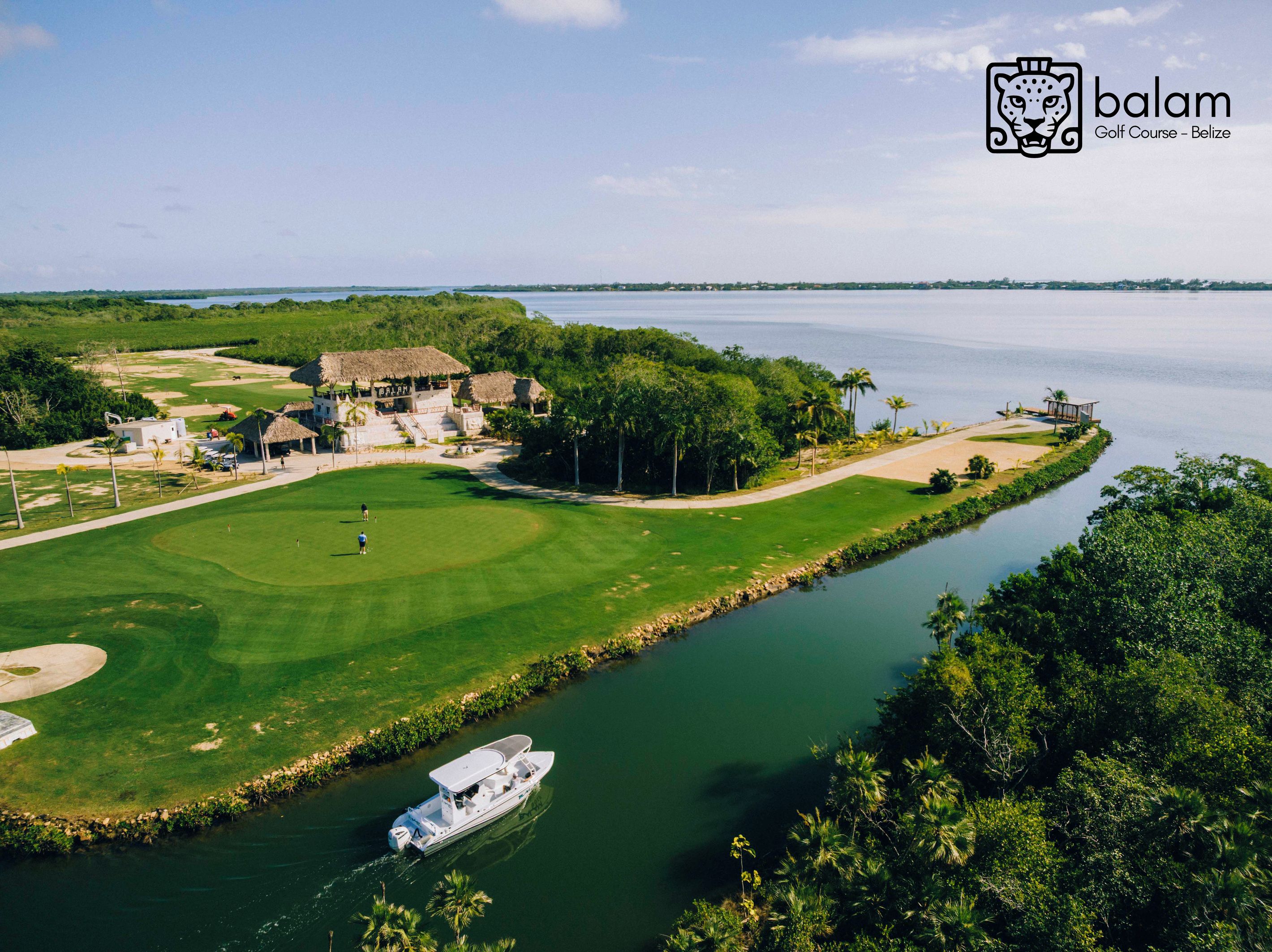 A golf course with a water body, a boat, and a building with a thatched roof.