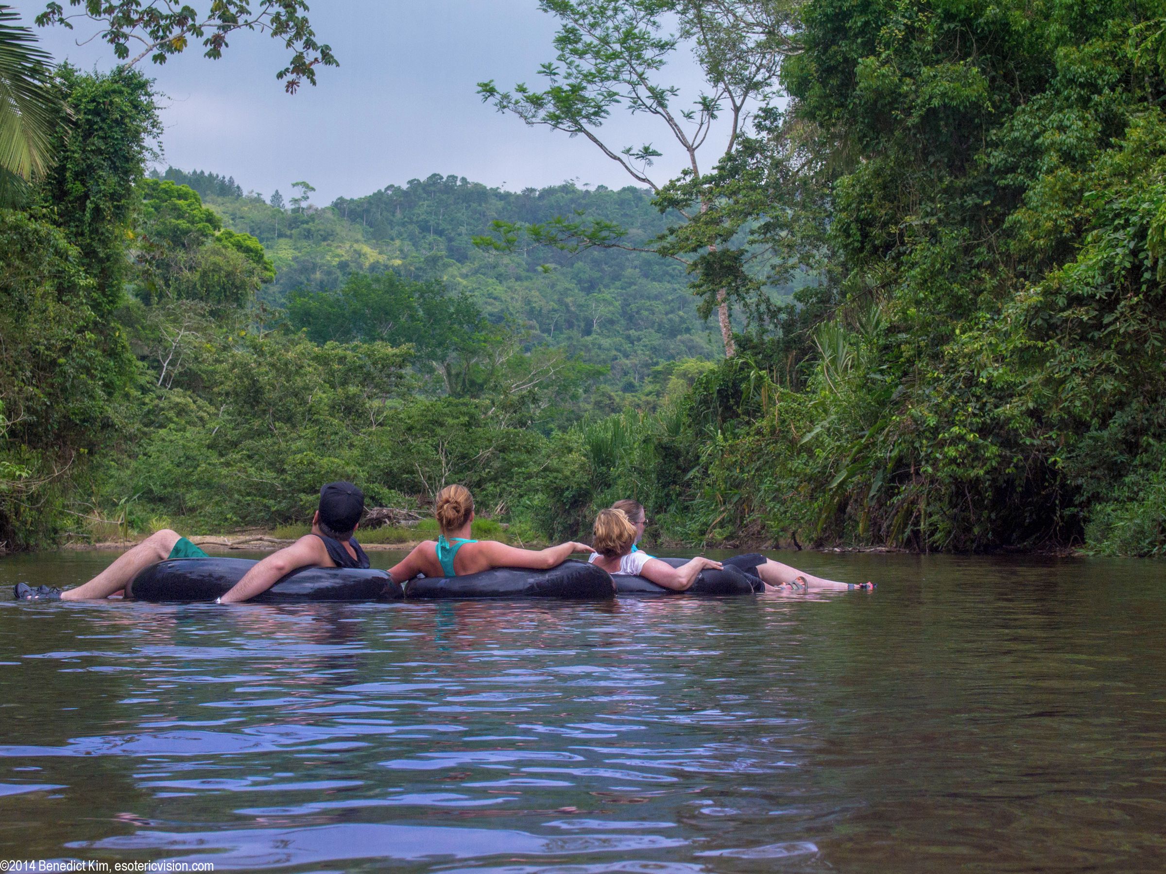 Drei Personen treiben in einem Fluss durch eine üppige, bewaldete Landschaft.