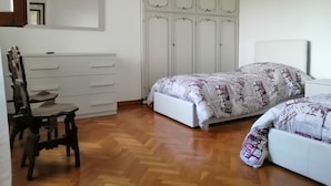 Een slaapkamer met houten vloer, een bed met behang, een stoel, een kapstok en een kledingkast.