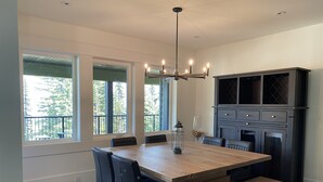 Un espace repas avec une grande table en bois, des chaises noires, un banc et un lustre.
