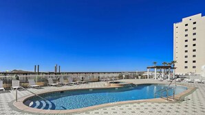 A swimming pool with a hexagonal tiled deck, lounge chairs, and a tall building in the background. - Newly remodeled and close to everything you need at Sea Glass Serenity.  (Navarre)