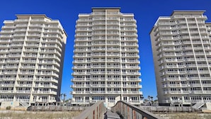 Three high-rise buildings with multiple balconies, a clear blue sky, and a pedestrian bridge in the foreground. - Newly remodeled and close to everything you need at Sea Glass Serenity.  (Navarre)