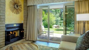 Ein Wohnzimmer mit Kamin, einer Couch und Blick auf einen Garten durch eine Schiebetür.