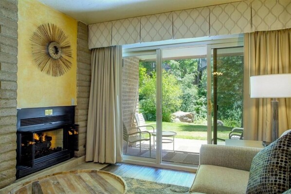 Ein Wohnzimmer mit Kamin, einer Couch und Blick auf einen Garten durch eine Schiebetür.
