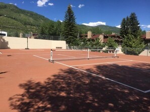 Ein Tennisplatz im Freien mit Netz, umgeben von Bäumen und Gebäuden.