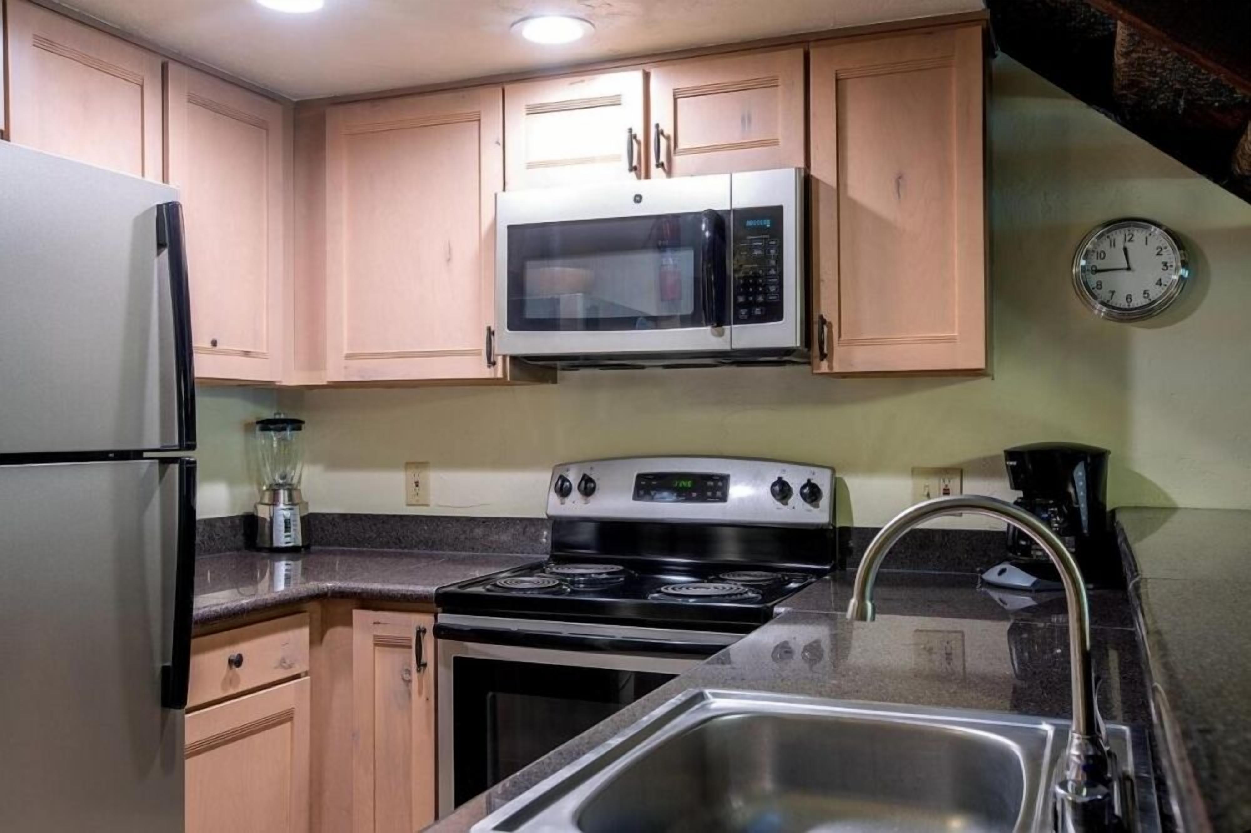 A kitchen with wooden cabinets, a stainless steel refrigerator, a microwave, a stove, and a sink.
