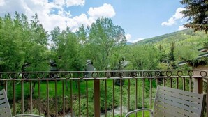 A balcony with metal railings overlooking a lush green landscape with trees and a small stream. - Bright & Sunny 2BR Condo with Jacuzzi & Tennis Court (Vail)