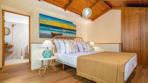 A bedroom with a wooden ceiling, a bed with a beige blanket, a nightstand with a lamp, a painting of a sunset over the ocean, and a wooden wardrobe. - Cottage Pearl-Rural Holiday Experience by SeaPearl.. (Paul do Mar - Calheta)