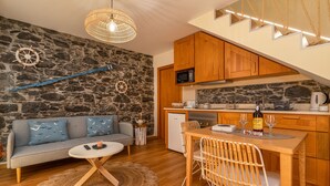 A cozy living area with a stone wall, a wooden dining table, and a sofa. - Cottage Pearl-Rural Holiday Experience by SeaPearl.. (Paul do Mar - Calheta)
