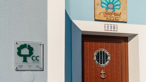 A wooden door with a circular window and an anchor decoration, a sign with a scallop shell and text, and a green certification label on the wall. - Cottage Pearl-Rural Holiday Experience by SeaPearl.. (Paul do Mar - Calheta)