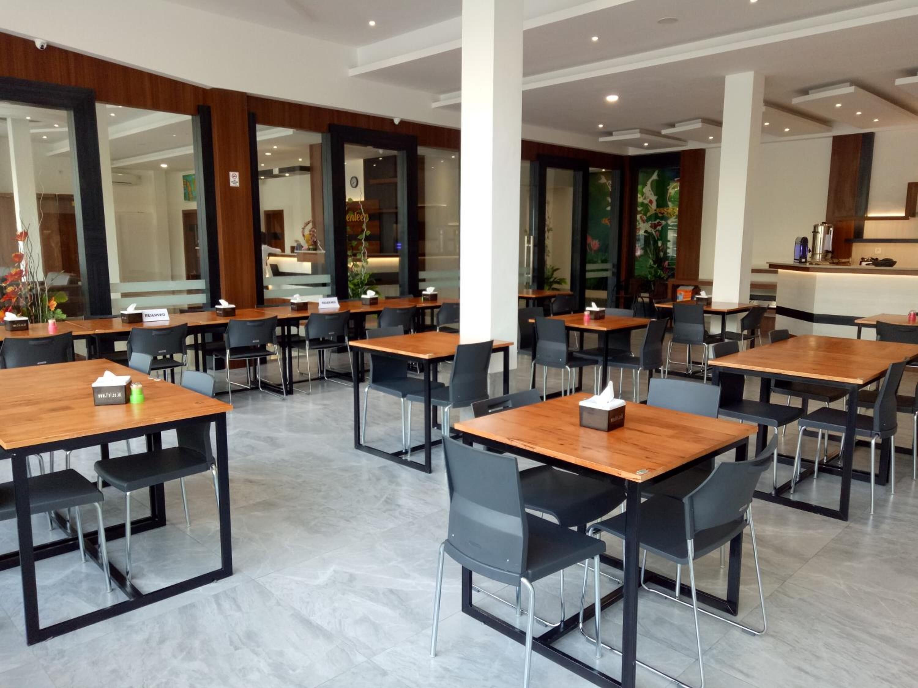 A modern dining area with wooden tables and black chairs, a reception desk, and a view of the interior.
