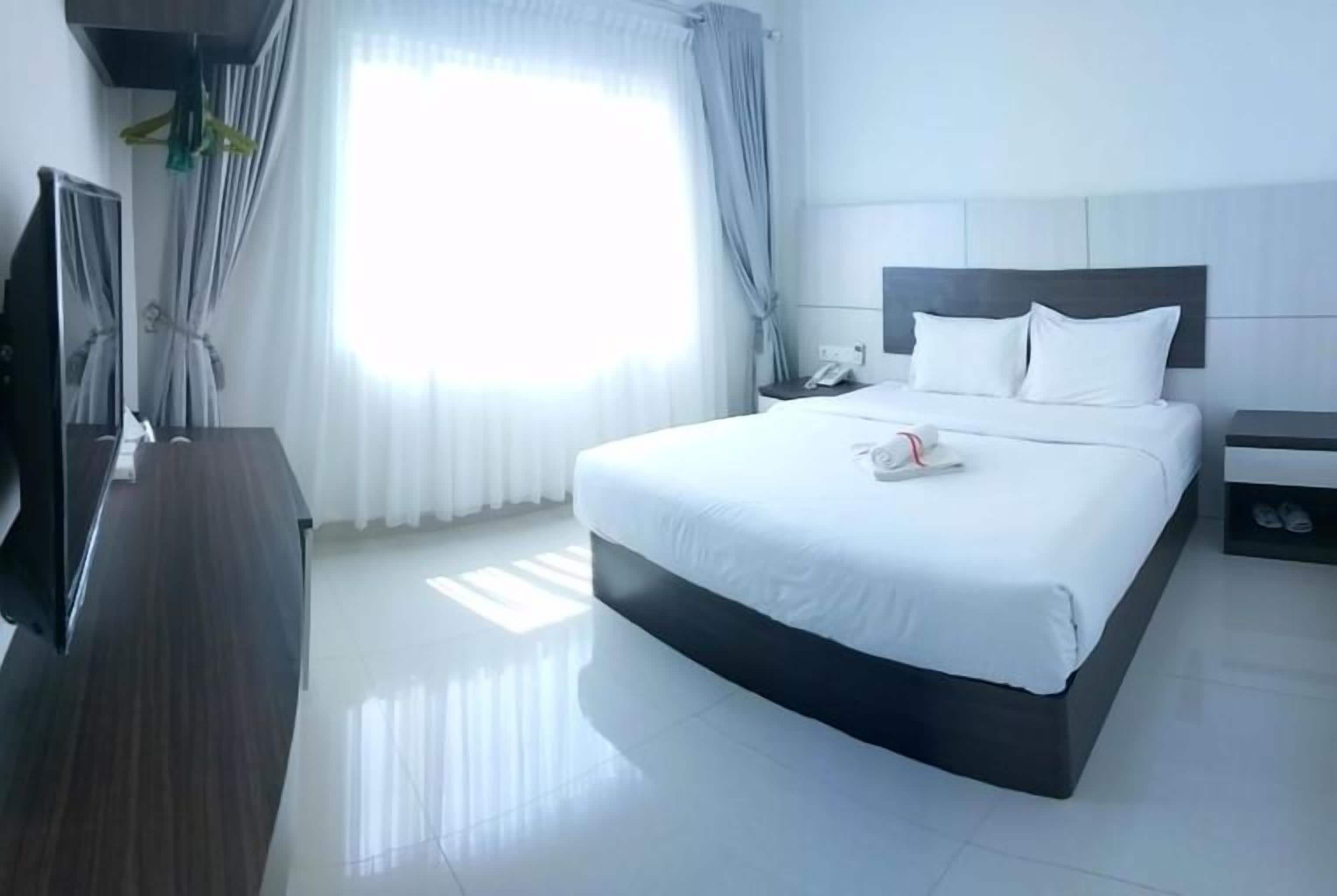 A hotel room with a large bed, bedside tables, a TV, and a window with curtains.