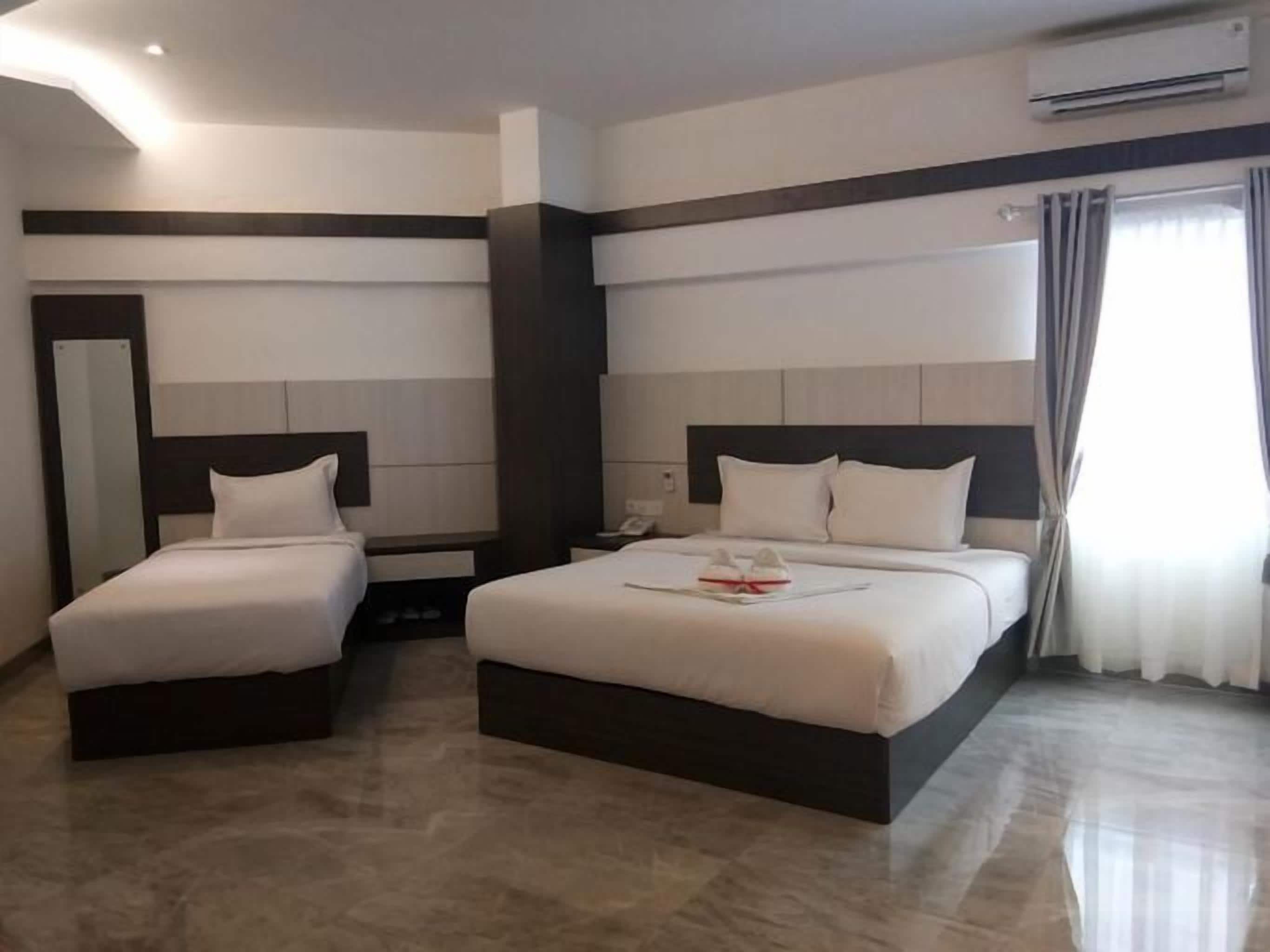 A hotel room with two beds, a bedside table, a mirror, and an air conditioning unit.
