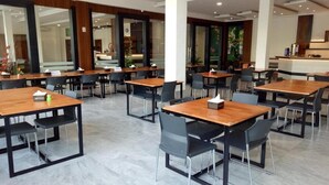 A modern dining area with wooden tables and black chairs, large windows, and a kitchen counter.