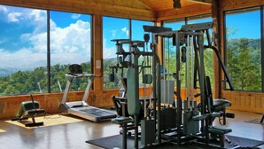 Un gimnasio con equipo de ejercicio y amplias ventanas con vistas a un paisaje boscoso.